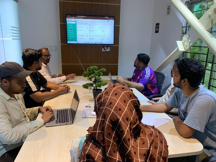 The Nanosoft team around a table with laptops, working through a dashboard on the wall screen.